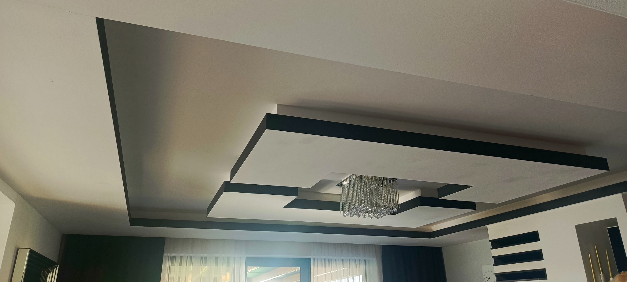 Nowoczesny sufit podwieszany z oświetleniem punktowym i listwami dekoracyjnymi w kolorze grafitowym, tworzący geometryczny wzór. Wykończenie wnętrza.