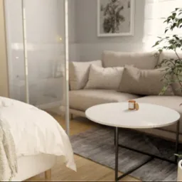 Jasna sypialnia z beżową sofą, okrągłym stolikiem i rośliną doniczkową. Minimalistyczny wystrój, naturalne światło. Widok na łóżko z miękką narzutą.