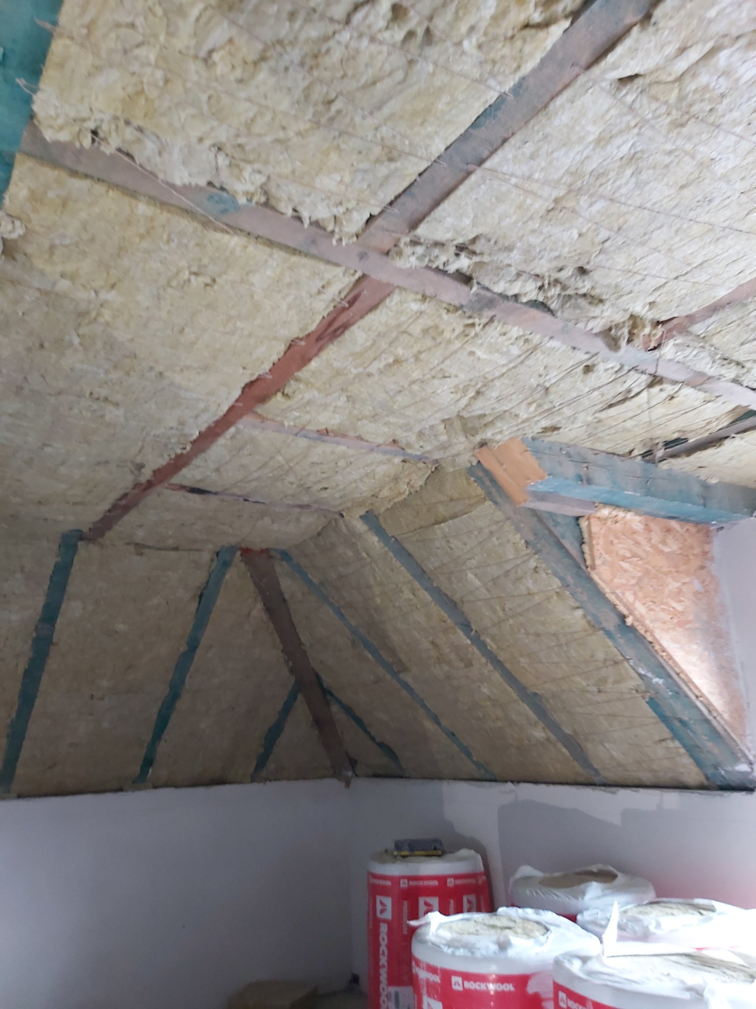 Poddasze w trakcie ocieplania wełną mineralną, widoczne drewniane belki konstrukcyjne i rolki wełny Rockwool na podłodze.