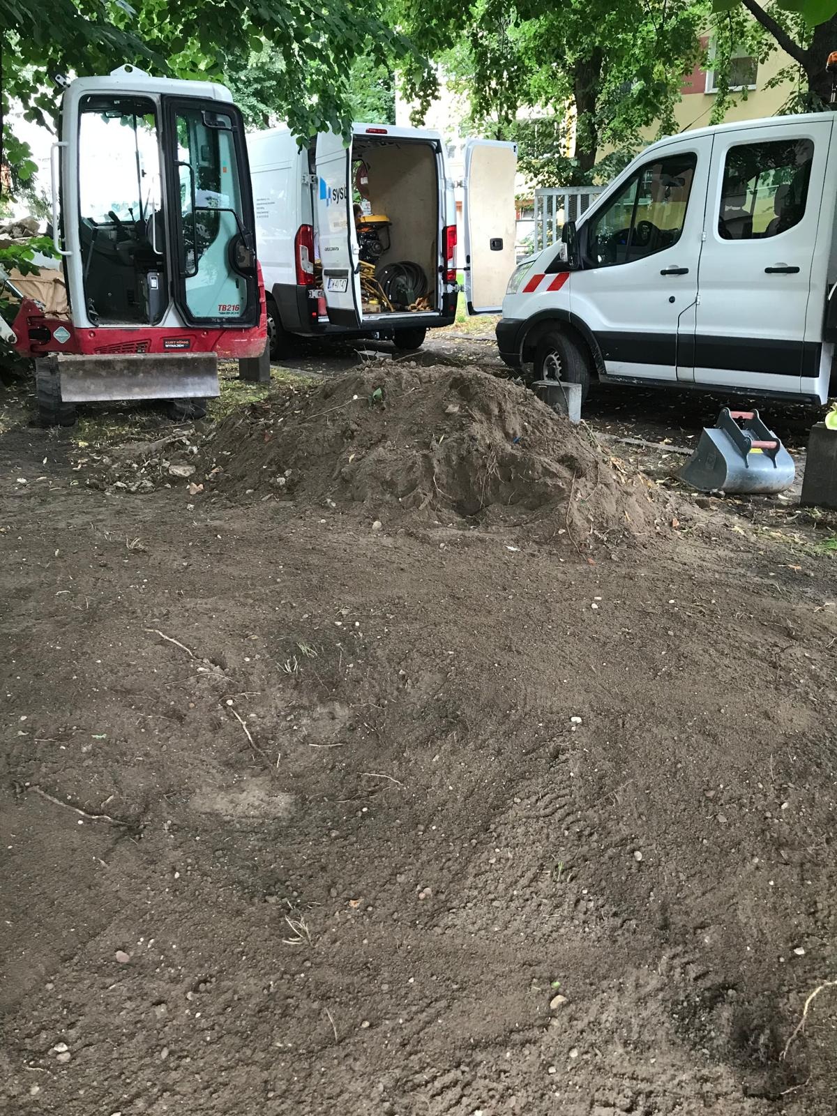 Wykop pod instalacje: Mini koparka TB216 oraz dwa busy na tle zieleni miejskiej, ziemia usypana w pryzmę. Widoczne ślady opon i narzędzie do kopania.