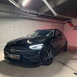 Leasing samochodów AutoPakiet - najem długoterminowy, kredyt na samochód - Czarny Mercedes-Benz kombi w garażu podziemnym, widok z przodu, reflektory włączone, oświetlenie sufitowe i numer stanowiska 26 w tle.