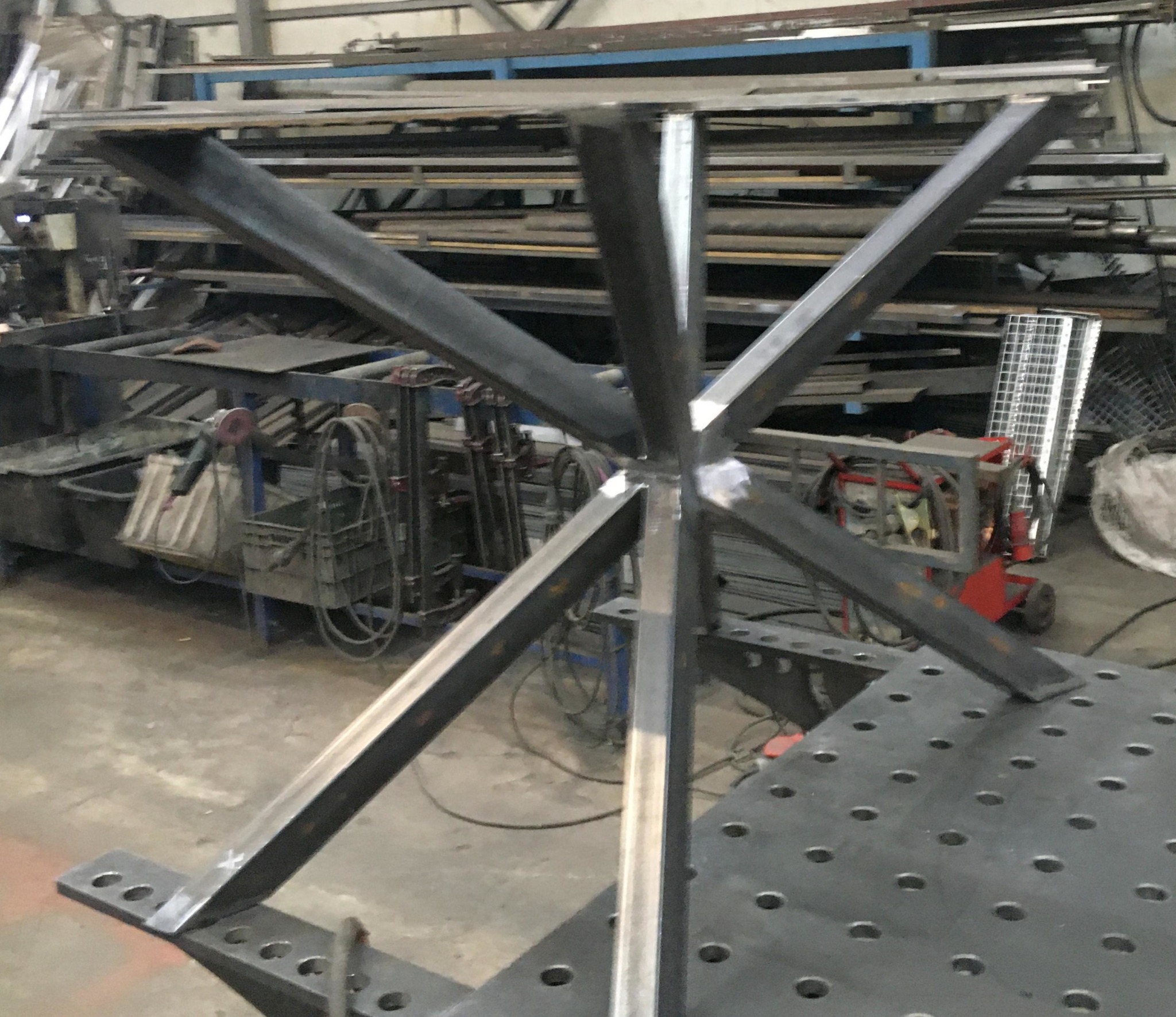 Surowa, spawana konstrukcja stalowa w warsztacie. Element podstawy stołu z profili. Widoczne spawy i perforowany stół spawalniczy.