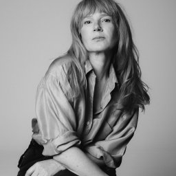 EWA POTOCZNA ConcEPt - Czarno-białe, studyjne ujęcie kobiety z długimi włosami w satynowej koszuli. Skrzyżowane ręce, stonowane tło, naturalny wyraz twarzy.