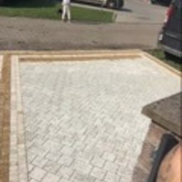 DDK BUD - Ułożona kostka brukowa w jasnych odcieniach, obramowana kostką w kolorze piaskowym. W tle zaparkowany bus i osoba w białym kombinezonie.