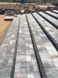 Ułożona szara kostka brukowa z ciemnymi pasami oddzielającymi, widok z góry, teren przygotowany do dalszych prac, w tle ziemia i materiały budowlane.