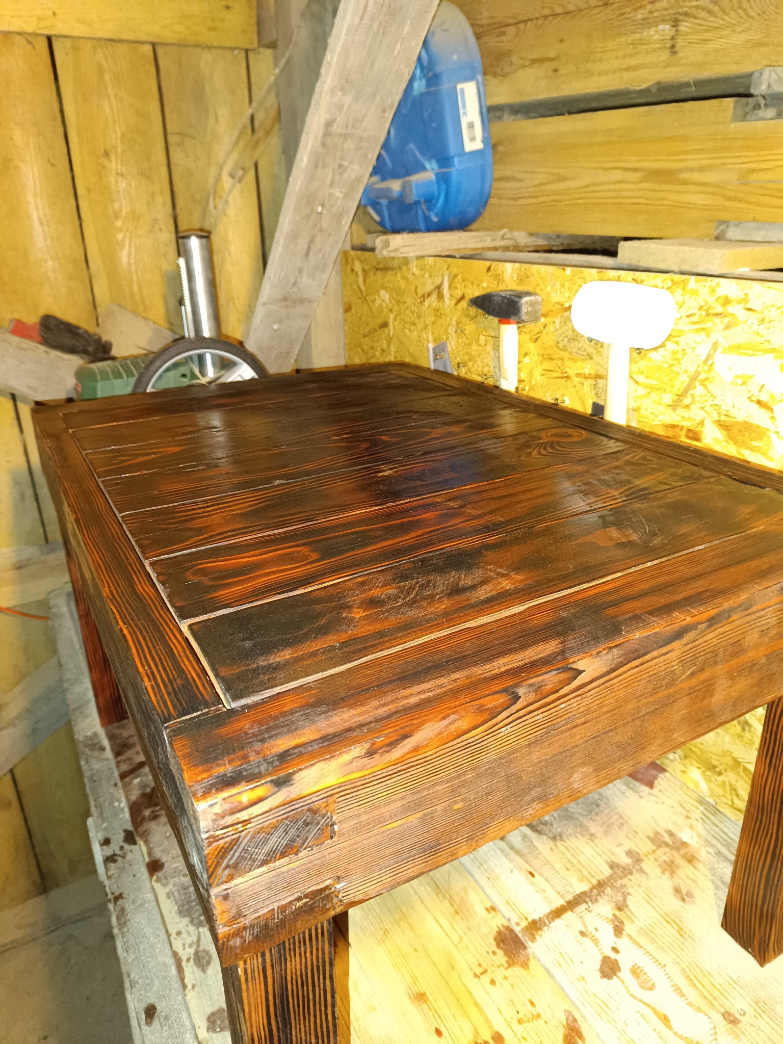 Ciemnobrązowy, lakierowany stolik kawowy z drewna, z widocznymi słojami, w warsztacie stolarskim. W tle narzędzia i materiały.