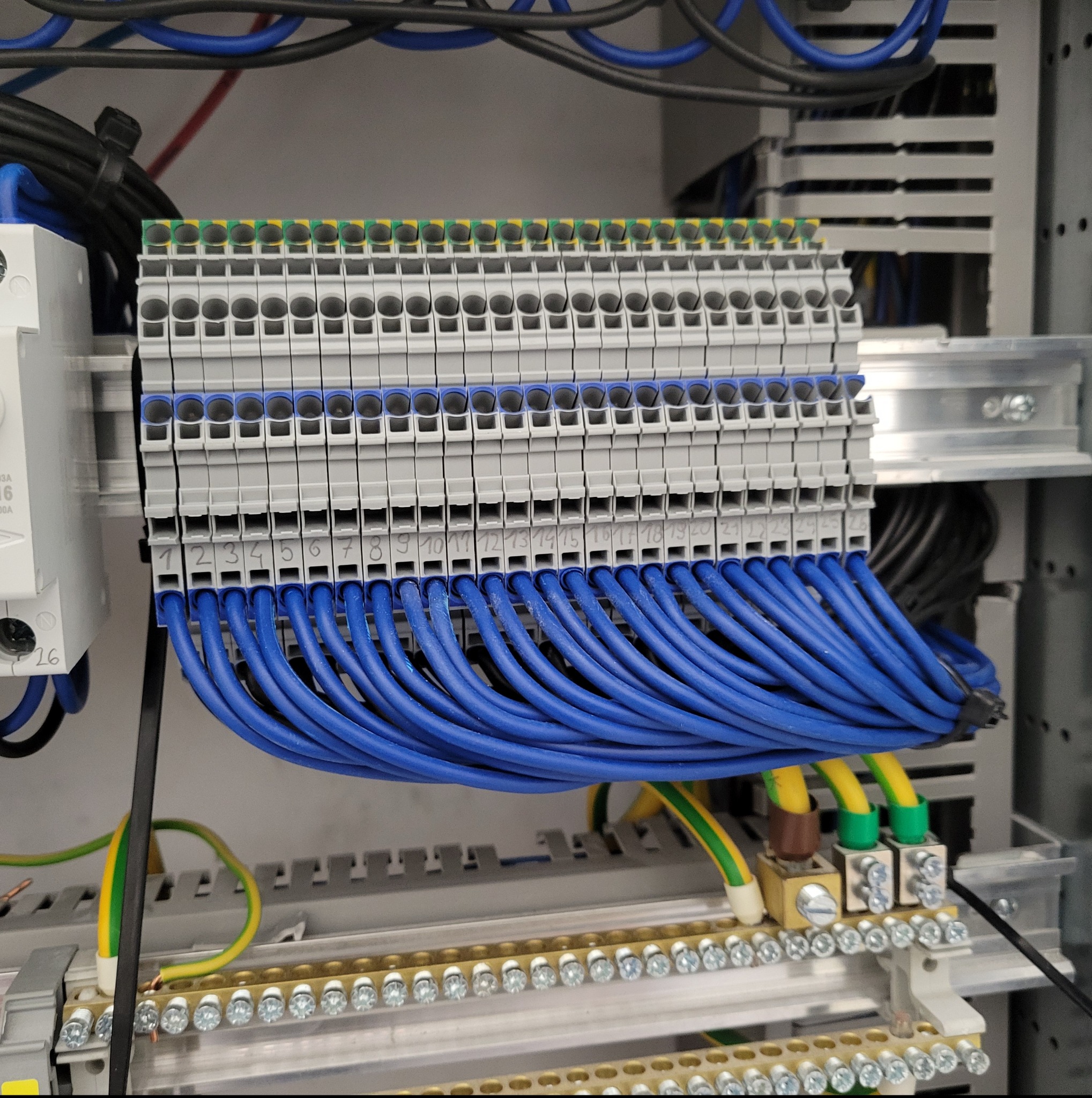 Szczegółowe ujęcie rozdzielnicy elektrycznej z precyzyjnie podłączonymi przewodami w kolorze niebieskim i żółto-zielonym, z numeracją od 1 do 26.