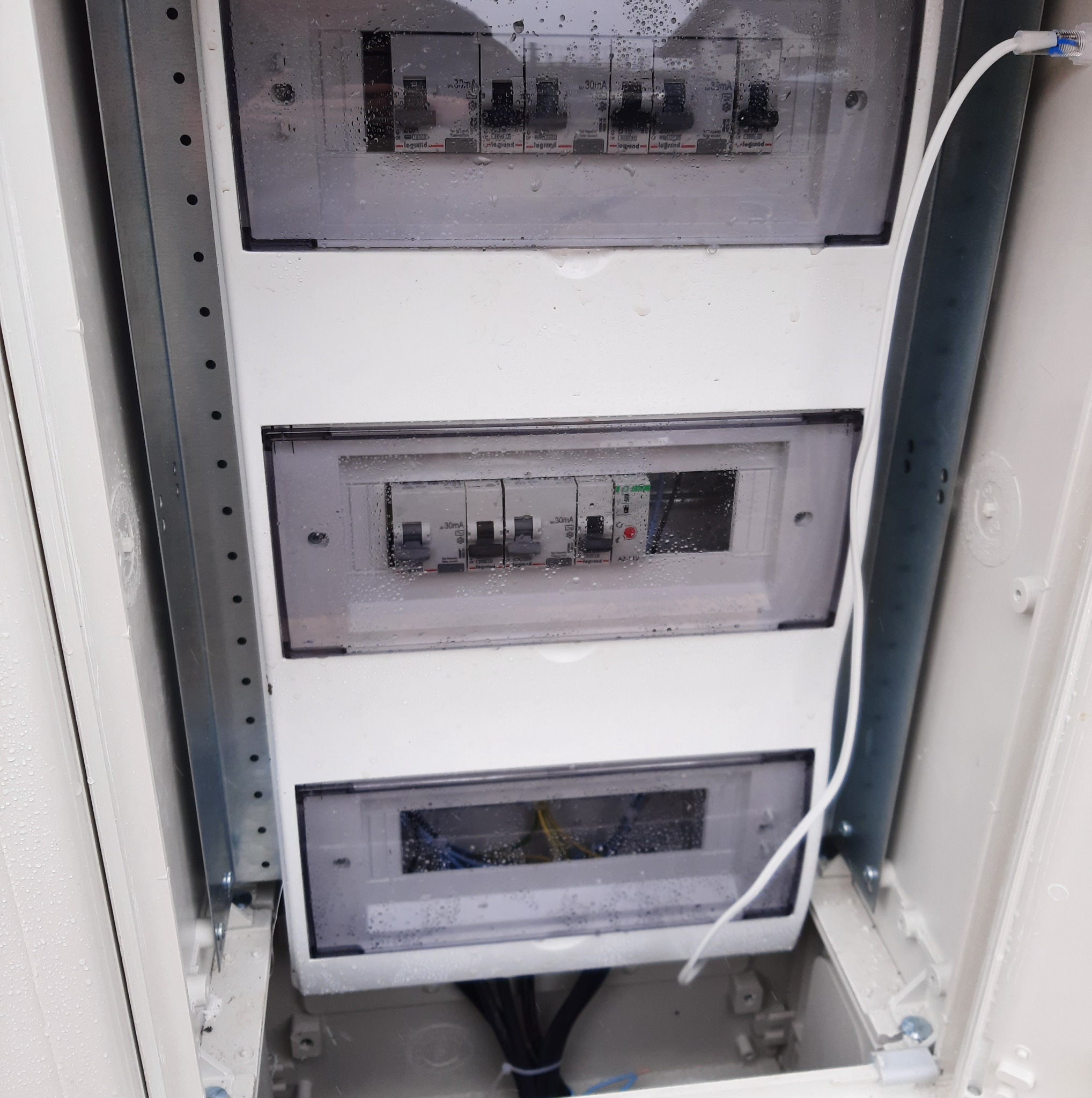 Rozdzielnia elektryczna z zamontowanymi bezpiecznikami Legrand, widoczna instalacja przewodów. Skrzynka zabezpieczona przed wilgocią. Element instalacji elektrycznej.