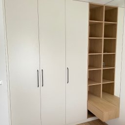 DJ Meble - Biała szafa wnękowa z czarnymi uchwytami i drewnianym regałem z lustrem. Minimalistyczny design, jasne wnętrze, parkiet na podłodze.