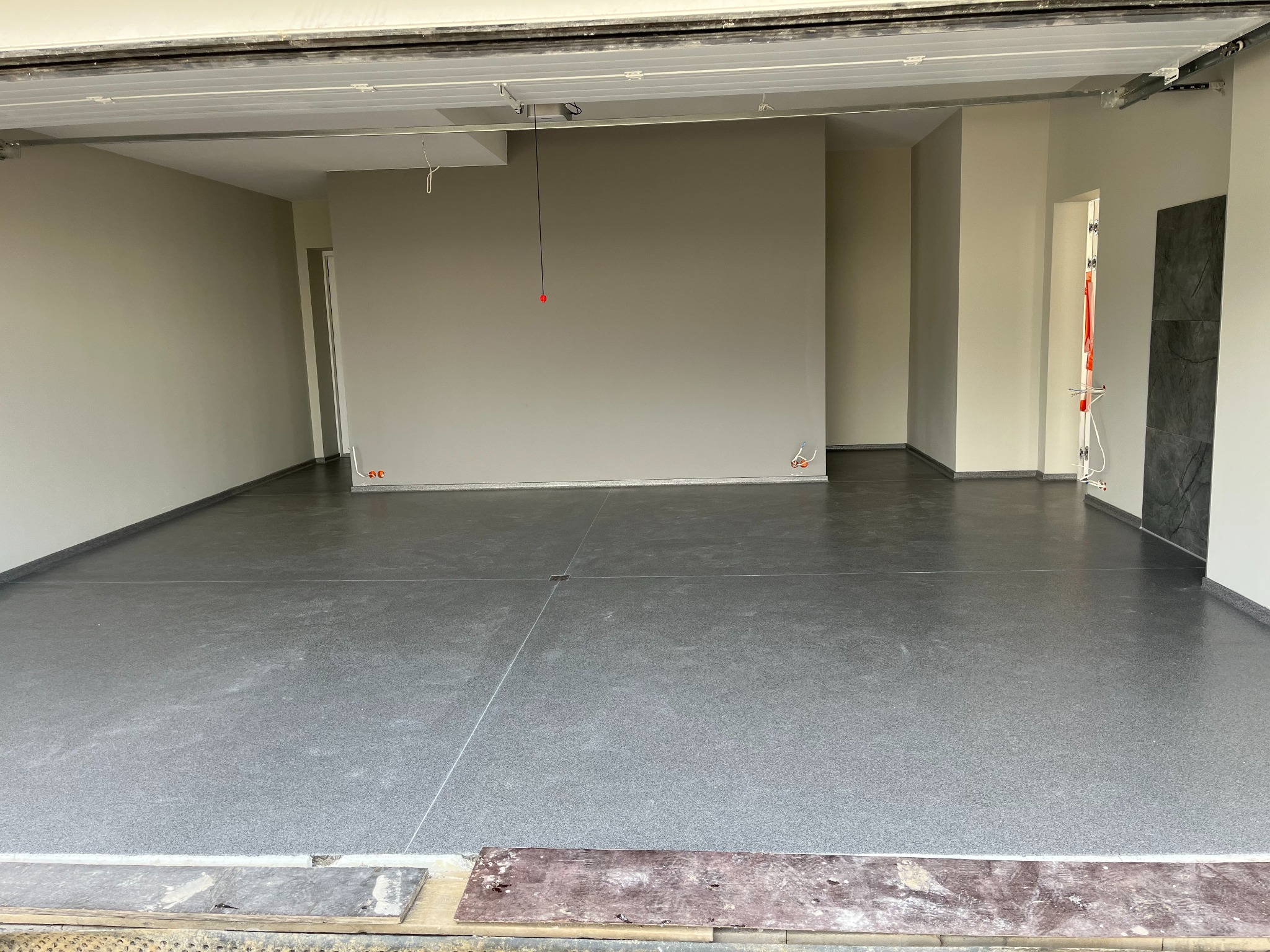 Szara, antypoślizgowa posadzka epoksydowa z cokolikiem w garażu. Widoczne wyoblenia przy ścianach i piasek kwarcowy w strukturze. Otwarta brama garażowa.