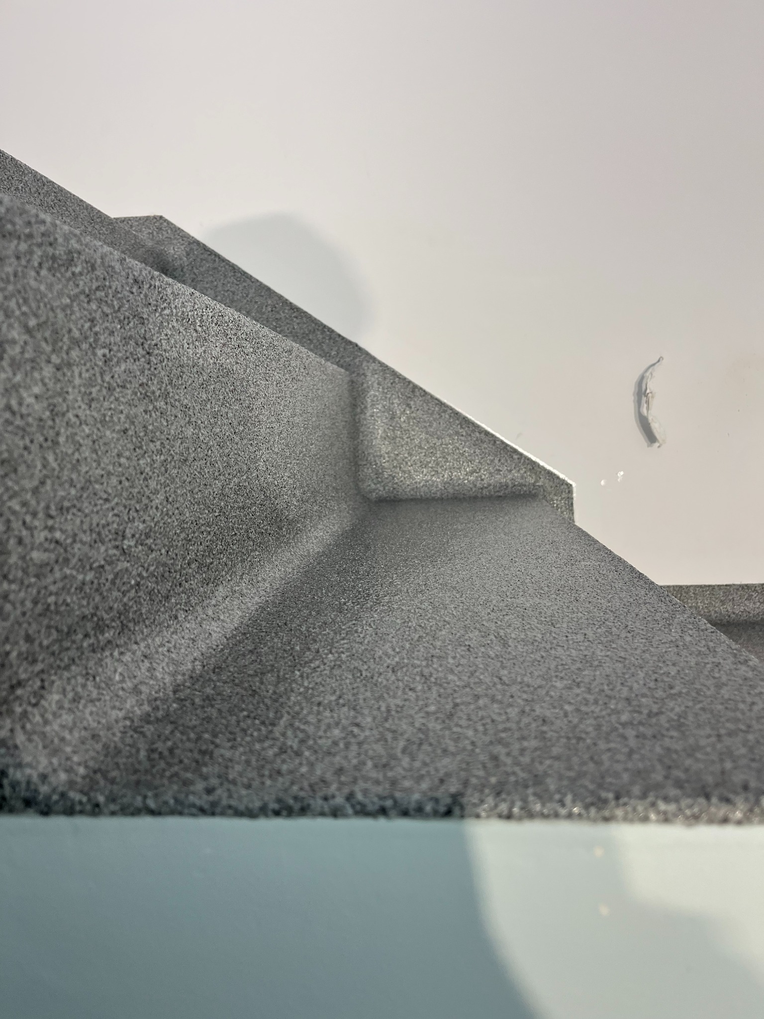 Szare schody z wykończeniem o fakturze kamienia, widok z dołu, z bliska. Na ścianie widoczny ślad po tapecie. Minimalistyczne ujęcie.