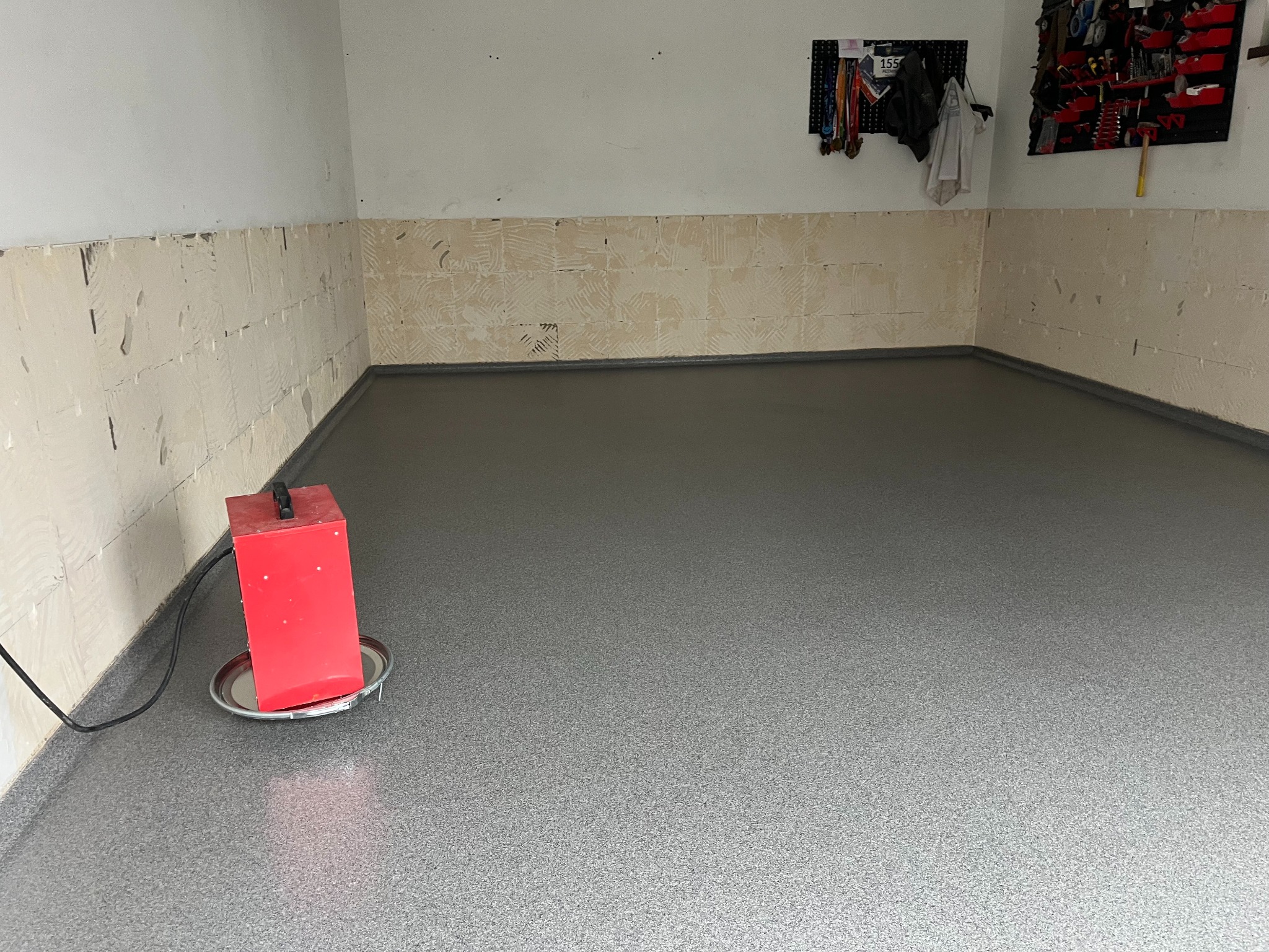Szara, antypoślizgowa posadzka epoksydowa z cokolikiem w garażu w Bytomiu. Widoczny czerwony agregat i ściany przygotowane pod dalsze prace wykończeniowe.