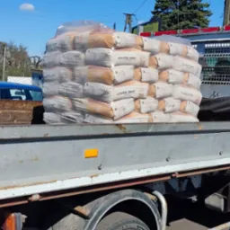 Ciężar&oacute;wka z workami cementu marki G&oacute;rażdże Cement Master na skrzyni ładunkowej. Widoczne numery kontaktowe na kabinie i otoczenie składu budowlanego.