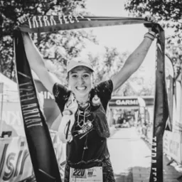 Uśmiechnięta kobieta z numerem 220 na mecie biegu Tatra Fest, z podniesionymi rękami trzyma baner. Czarno-białe zdjęcie z widocznym logiem Garmin w tle.