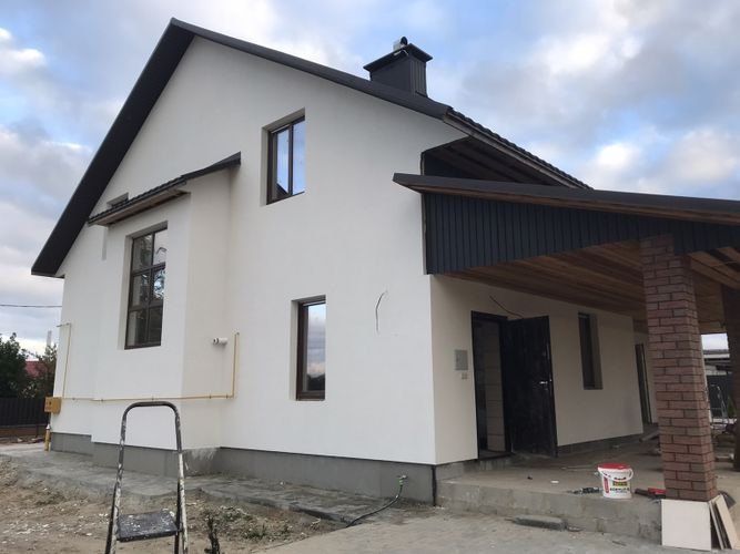 Dom jednorodzinny z białą elewacją i ciemnymi elementami wykończeniowymi, widoczna drabina i wiadro farby, sugerujące świeżo wykonane prace elewacyjne.