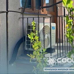 Cool Solutions Dawid Mochocki - Zamontowana jednostka zewnętrzna klimatyzacji na balkonie w Goleszowie. Widoczny czarny peszel i fragment balustrady. Częściowo zasłonięte przez roślinę.