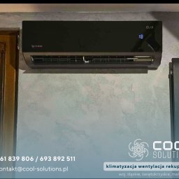 Cool Solutions Dawid Mochocki - Czarny klimatyzator Rotenso Elis zamontowany na ścianie o fakturze betonu, obok grzejnika. Widoczny numer 18 na wyświetlaczu. Ujęcie z bliska.