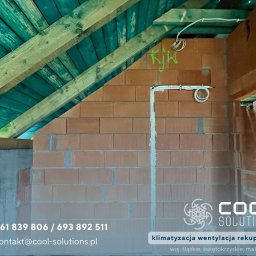 Cool Solutions Dawid Mochocki - Instalacja przewodów wentylacyjnych na ceglanej ścianie poddasza z drewnianą konstrukcją dachu. Widoczne elementy systemu wentylacji.
