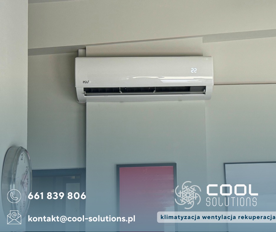 Biała klimatyzacja ścienna w nowoczesnym wnętrzu, widoczny zegar i obrazy w tle, z logo firmy COOL SOLUTIONS. Wyświetlacz pokazuje temperaturę 22 stopnie.