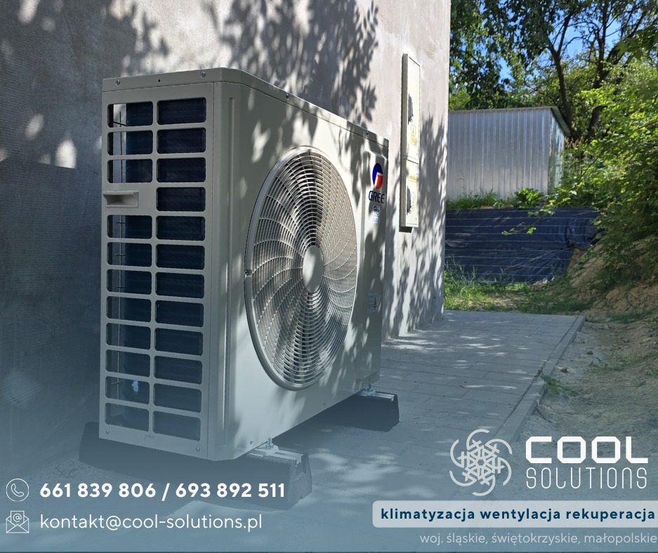 Zamontowana jednostka zewnętrzna klimatyzacji Gree na betonowej podstawie, na tle ściany budynku z cieniem drzewa i zieleni w tle. Widoczny fragment logo firmy.