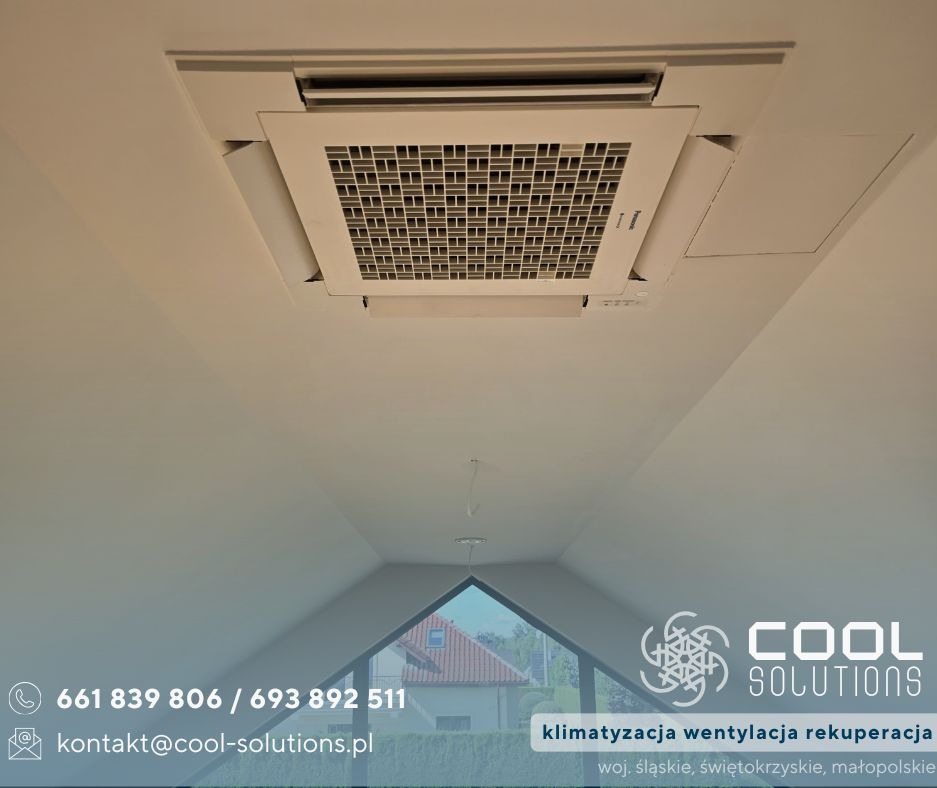 Kasetonowa klimatyzacja sufitowa w jasnym pomieszczeniu na poddaszu. Widoczny fragment okna i logo firmy Cool Solutions w dolnej części zdjęcia.