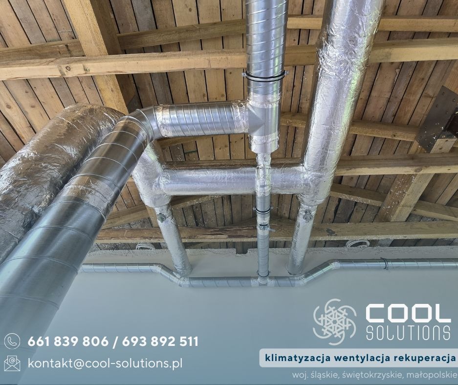 Montaż wentylacji pod drewnianym stropem. Srebrne, izolowane rury wentylacyjne rozchodzą się pod sufitem. Widoczny fragment logo firmy Cool Solutions.