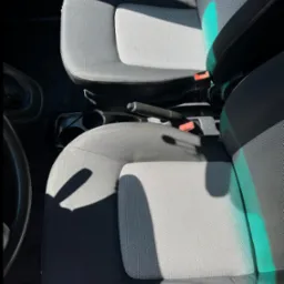 Szare, tekstylne fotele samochodowe z widocznymi pasami bezpieczeństwa i elementami deski rozdzielczej, oświetlone naturalnym światłem słonecznym.