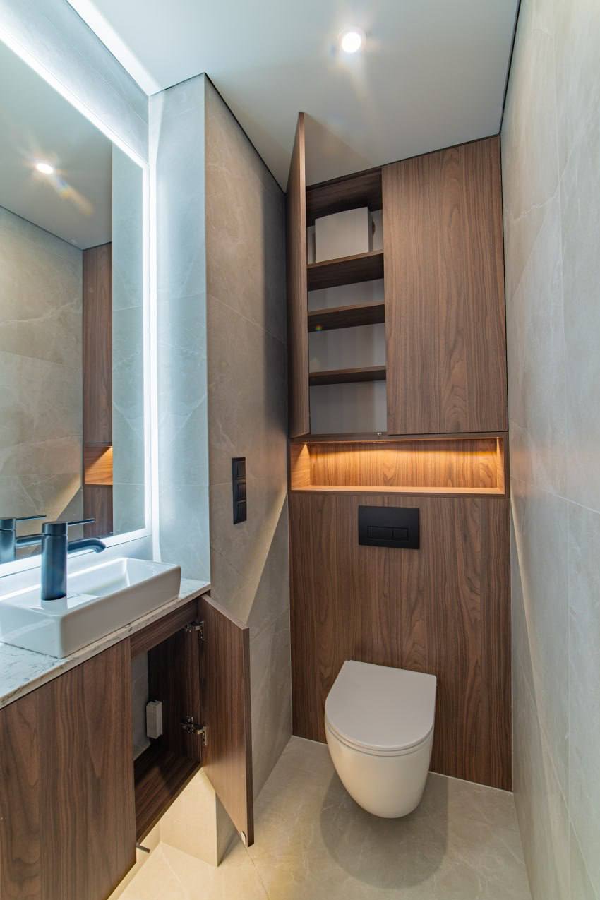 Nowoczesna łazienka z podświetlanym lustrem, szafką z drewnianym fornirem i podwieszaną toaletą. Minimalistyczny design, szare płytki imitujące marmur.