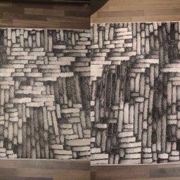 Czystoneo - Wzór dywanu z abstrakcyjnym motywem cegieł w odcieniach szarości i bieli, leżący na panelach podłogowych. Widok z góry, fragment dywanu.