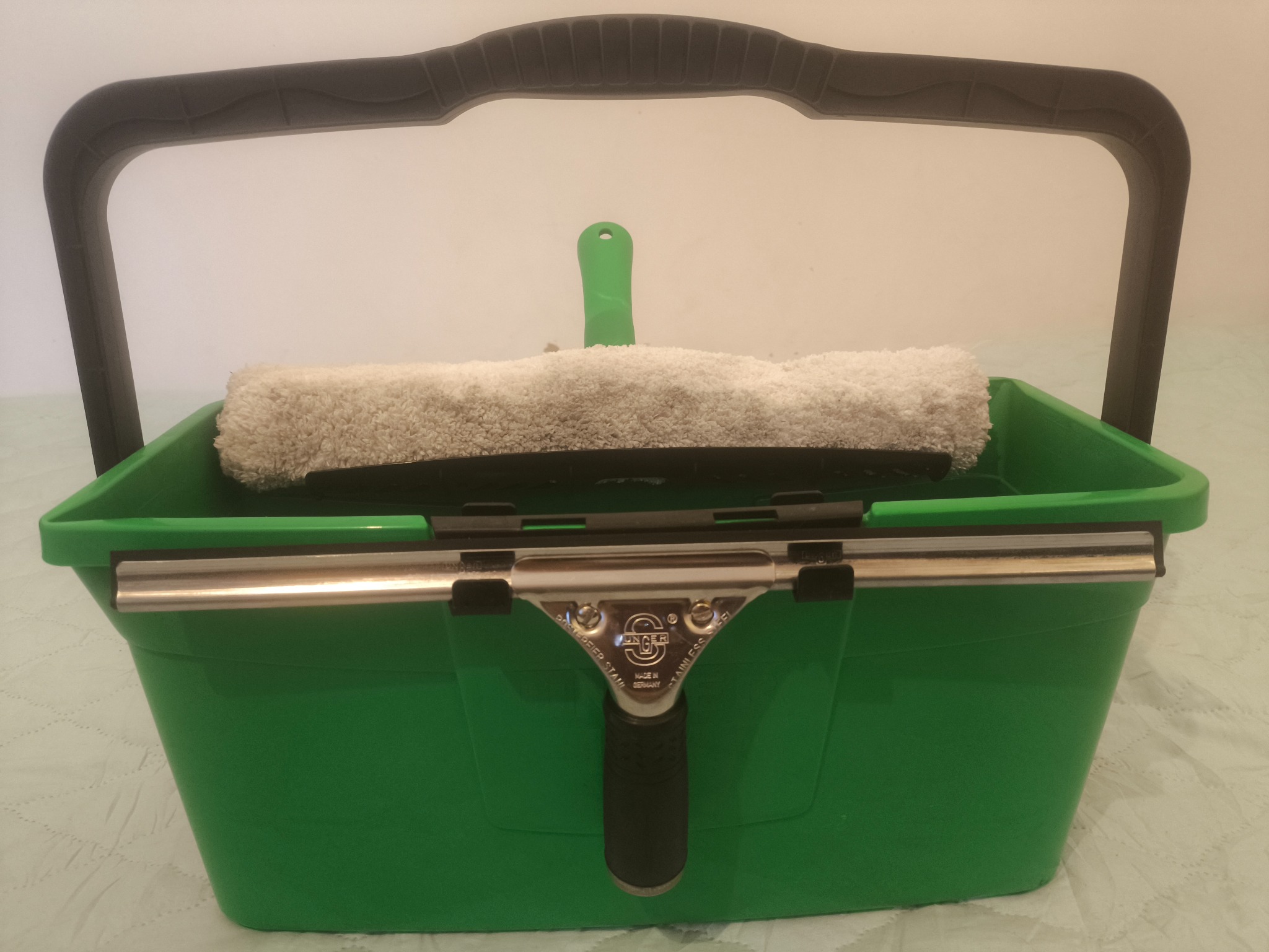 Zielone wiadro z uchwytem, wewnątrz mop do mycia okien i ściągaczka Unger. Sprzęt do mycia okien.