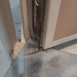 Szczeg&oacute;łowe ujęcie styku ościeżnicy z podłogą, widoczne elementy montażowe i uszczelka, ukazujące precyzję wykonania. Widoczne drobne zabrudzenia.