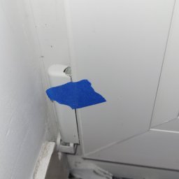 Michał Stępiński - Szczegółowe ujęcie uszkodzonego okna PCV z niebieską taśmą zabezpieczającą, ukazujące defekt i niedoróbki wykończeniowe przy podłodze.