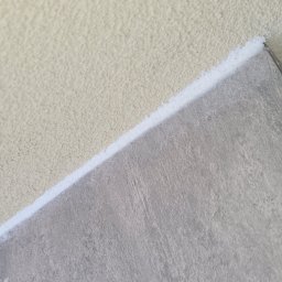 Michał Stępiński - Fragment ściany z nałożonym tynkiem strukturalnym i płytą. Widoczna biała warstwa izolacyjna pomiędzy nimi. Praca wykończeniowa w trakcie realizacji.