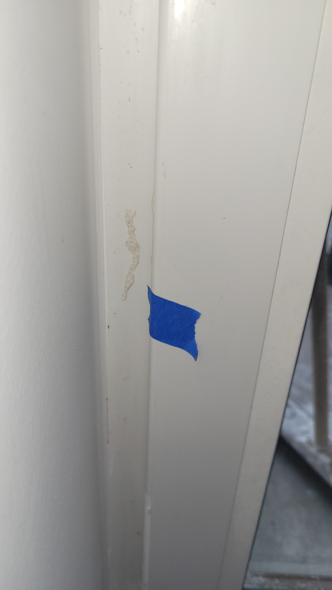 Fragment ściany z ubytkiem i niebieską taśmą malarską w Białymstoku, przygotowany do naprawy. Widoczne ślady po usuniętej farbie.