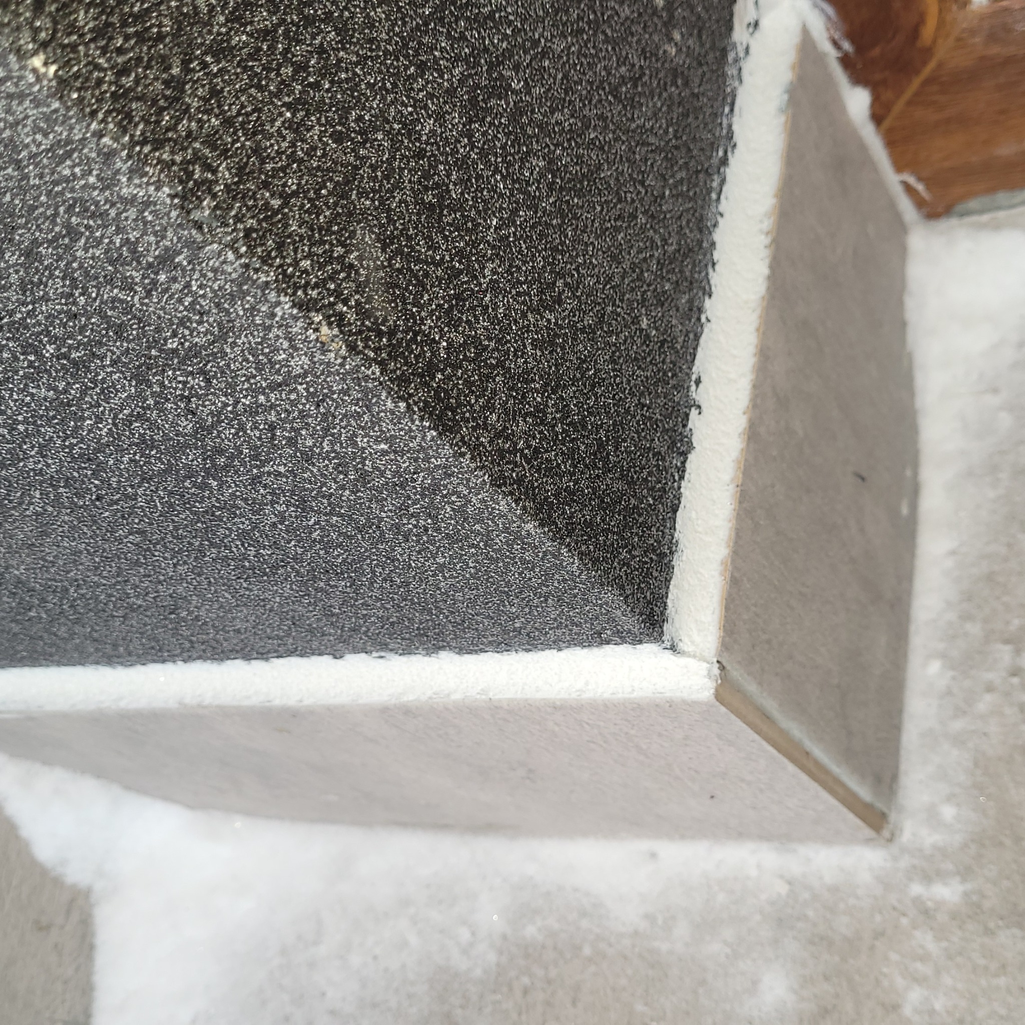 Fragment ocieplonego narożnika ściany z szarą płytą i pianką montażową. Widoczne nierówności i faktura materiałów. Ujęcie z bliska.