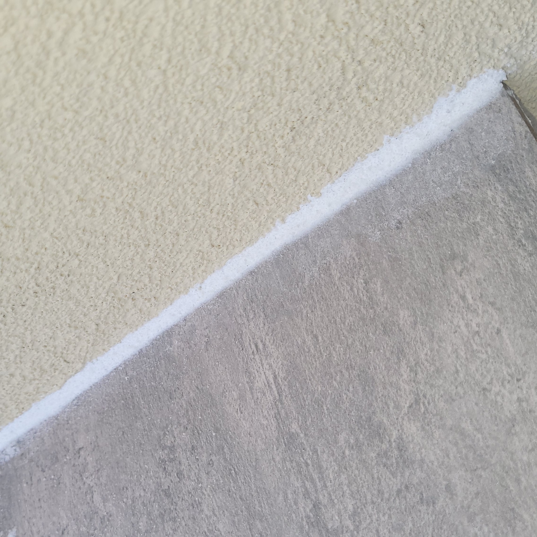 Fragment ściany z nałożonym tynkiem strukturalnym i płytą. Widoczna biała warstwa izolacyjna pomiędzy nimi. Praca wykończeniowa w trakcie realizacji.