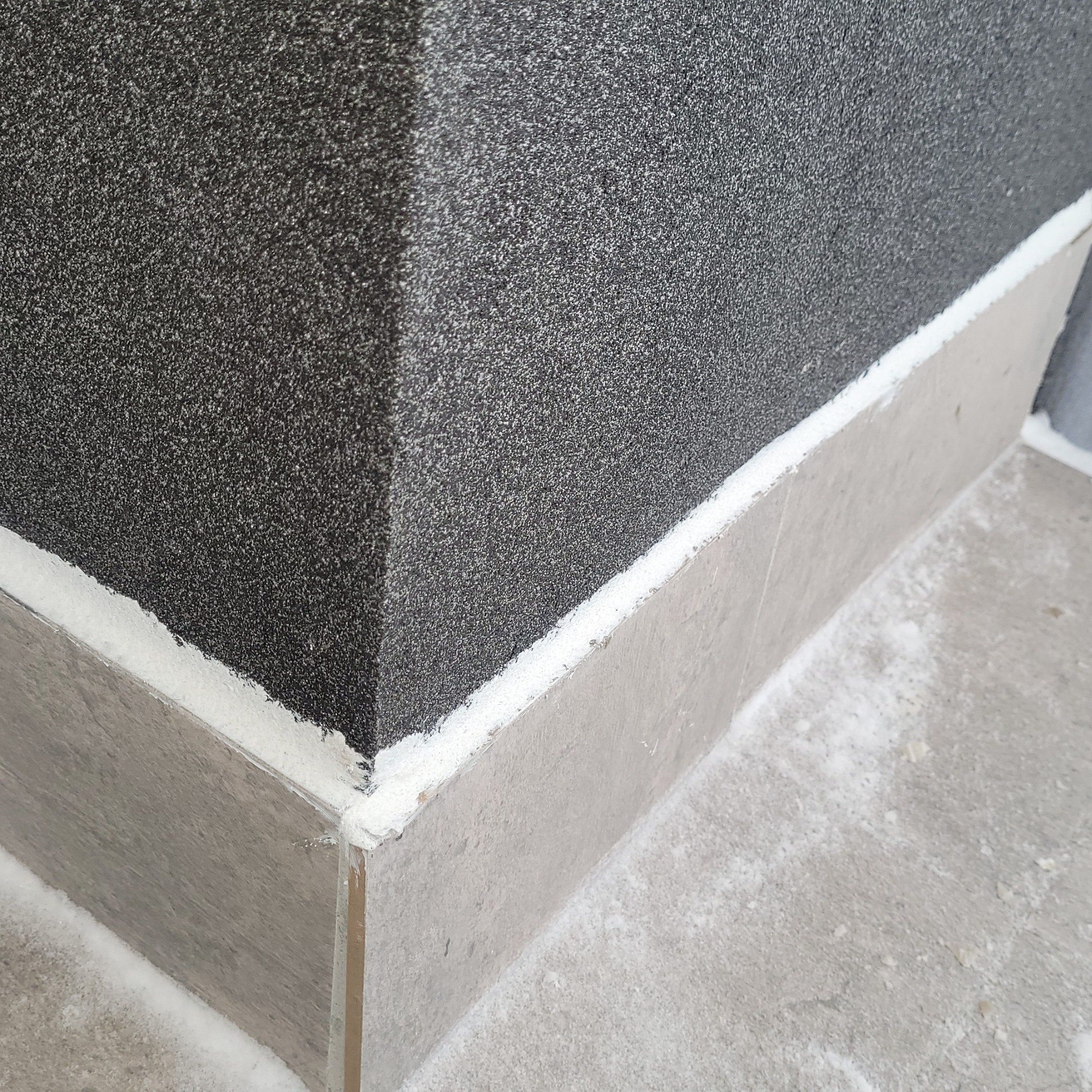 Szaro-czarna elewacja budynku z dekoracyjnym cokołem z płytek, wypełniona białą fugą. Widoczny narożnik i fragment posadzki.