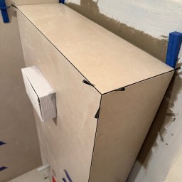 M&D Remont4everyone Mykola Petruniv - Fragment obudowy z płytek w trakcie montażu, z użyciem poziomujących klinów i krzyżyków dystansowych, widoczne surowe ściany w tle.