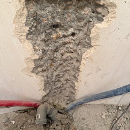 M&D Remont4everyone Mykola Petruniv - Odsłonięty fragment ściany z instalacją hydrauliczną w trakcie prac remontowych. Widoczne rury i gruz.