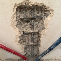 M&D Remont4everyone Mykola Petruniv - Odsłonięte zbrojenie w ścianie z instalacją hydrauliczną (czerwona i niebieska rura) oraz szarą rurą kanalizacyjną u dołu. Widoczne ślady po kuciu w tynku.