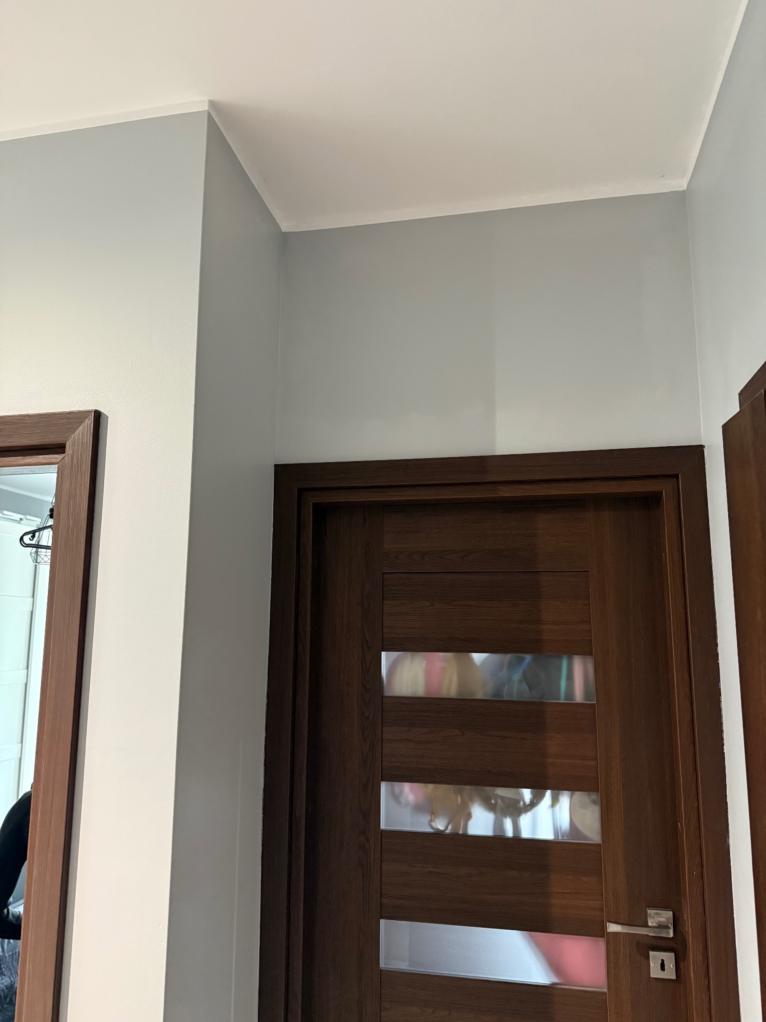 Wnętrze po malowaniu: szare ściany, biały sufit i drewniane drzwi z przeszkleniami. Widoczny fragment drugich drzwi z lustrem.