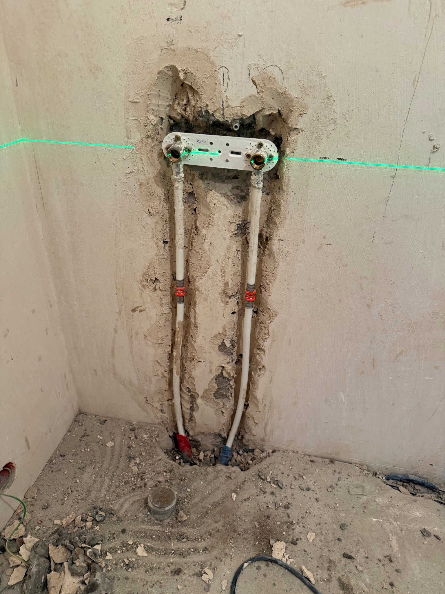 Montaż instalacji wodnej w łazience, widoczne rury i laserowy poziom na ścianie w trakcie prac. Surowy stan, przygotowanie do dalszych prac wykończeniowych.