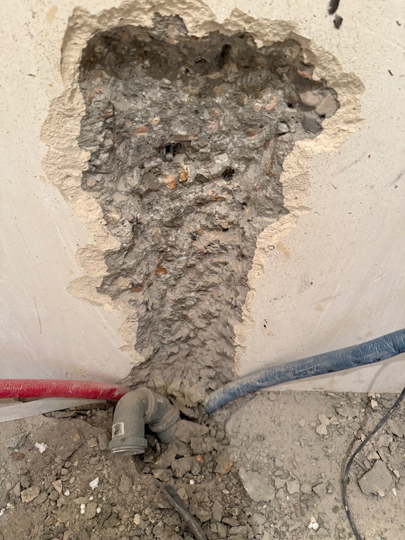 Odsłonięty fragment ściany z instalacją hydrauliczną w trakcie prac remontowych. Widoczne rury i gruz.