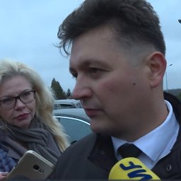 Adwokat Siedlce - Michał Wąż - Wywiad z prawnikiem: Mężczyzna w garniturze odpowiada na pytania dziennikarzy z mikrofonami, w tle kobieta z telefonem.