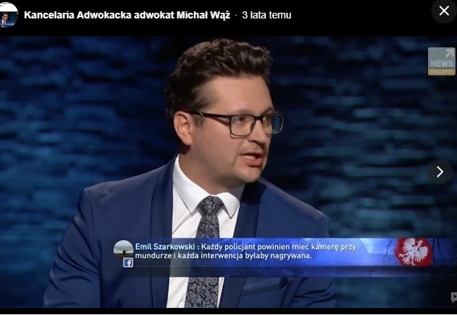 Adwokat Michał Wąż w studio telewizyjnym podczas wywiadu, ubrany w garnitur i okulary, na tle ciemnego studia z logo stacji Polsat News.