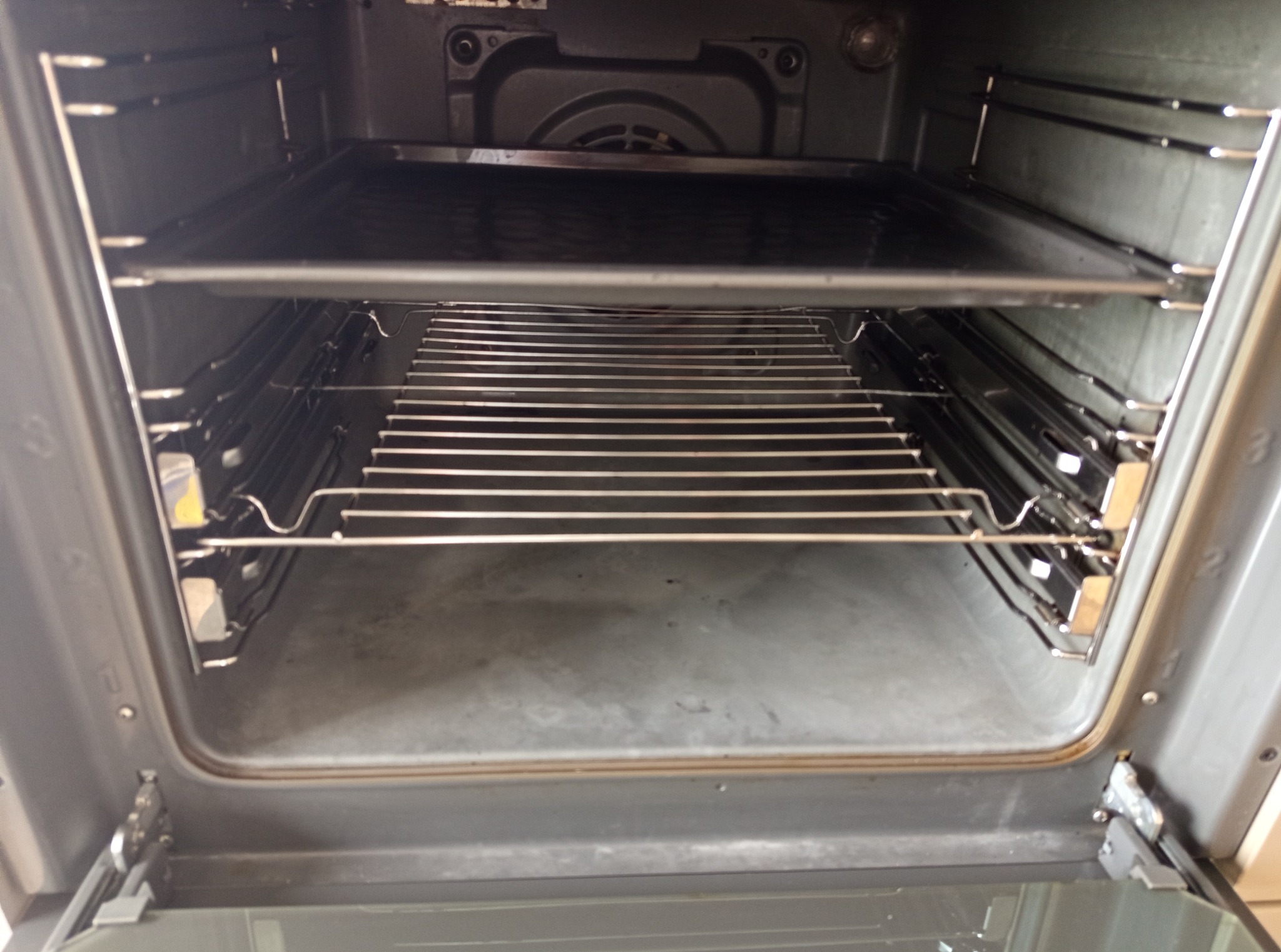 Wnętrze brudnego piekarnika z rusztem i blachą przed czyszczeniem, widok z przodu, szare wnętrze, metalowe elementy, resztki jedzenia.