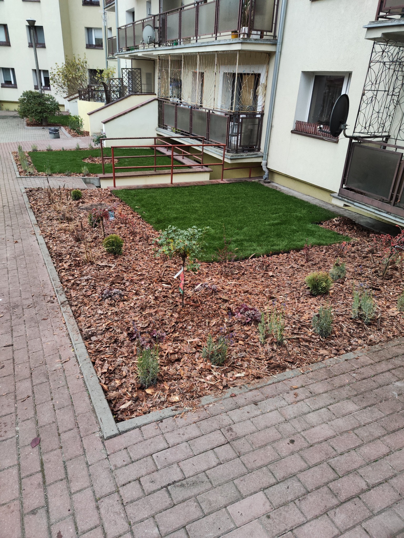 Estetyczne zagospodarowanie terenu: trawniki z rolki, nasadzenia roślin iglastych i rabaty wysypane korą, obrzeża trawników z kostki brukowej przy budynku.