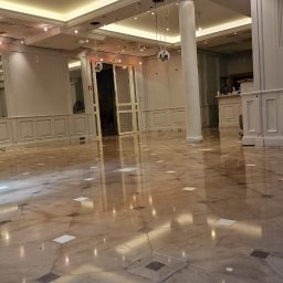 PROFCHEM Agnieszka Kozieł - Wypolerowana marmurowa podłoga w przestronnym, jasnym pomieszczeniu z kolumnami i oświetleniem sufitowym. Widoczne odbicia światła na powierzchni podłogi.