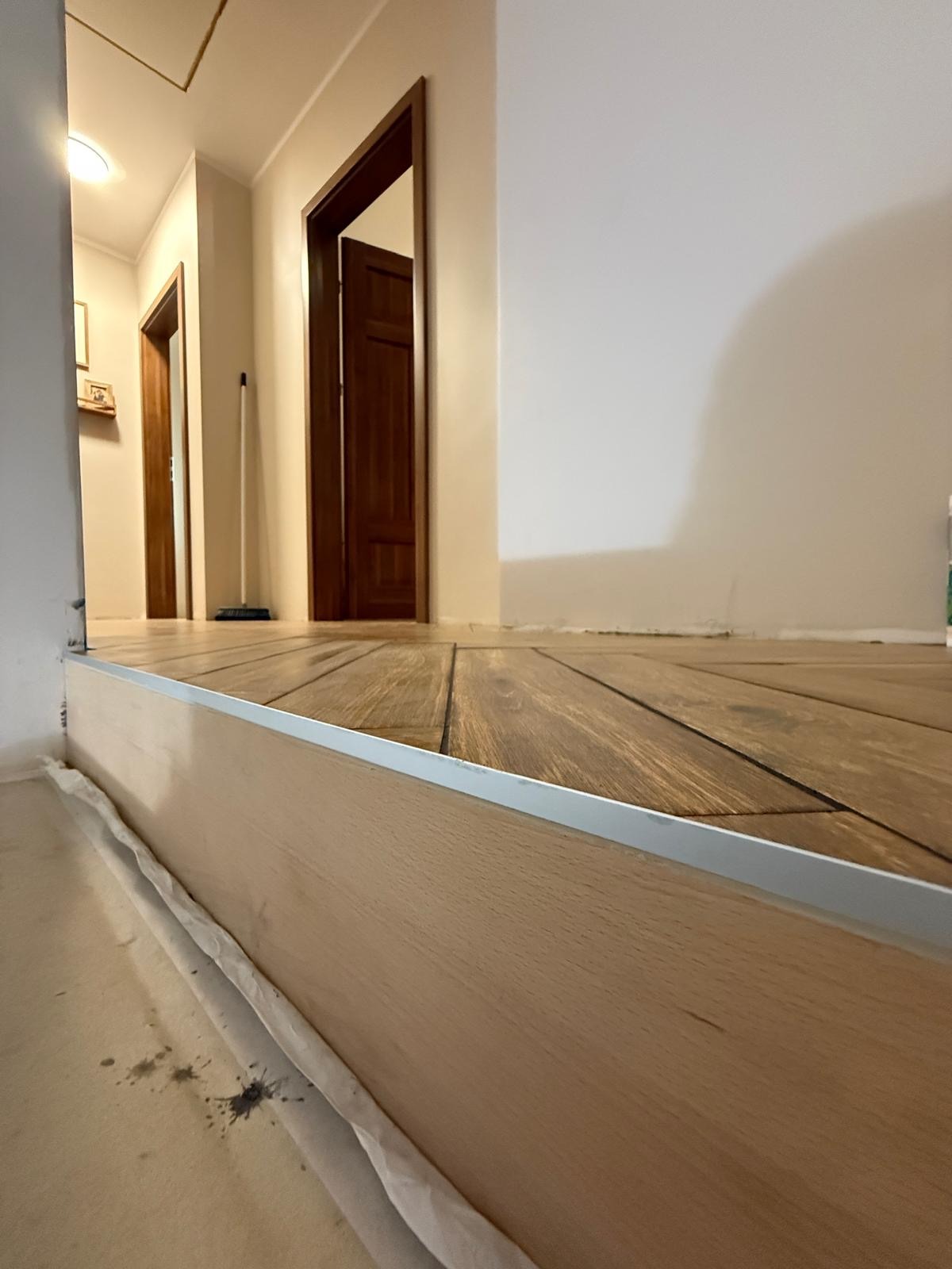 Ukończone drewnopodobne płytki podłogowe w korytarzu, z listwą przypodłogową i widocznymi drzwiami w tle. Ujęcie z niskiego kąta.