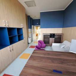 DesignLAB Manufaktura Mebli - Jasne, drewniane szafy z niebieskimi wnękami, fioletowe krzesła i drewniany stół w przestronnym wnętrzu z niebieskimi akcentami na ścianach.